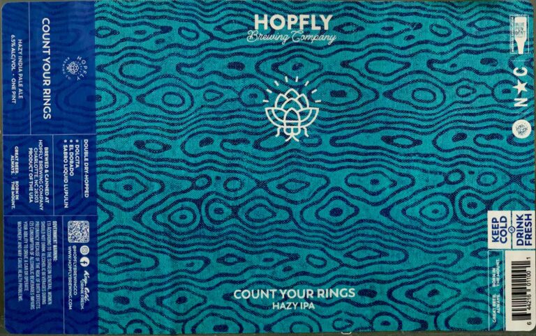 Count Your Rings beer label from Hopfly: A white hop cone icon centered on a teal background with dark wavy lines resembling wood grain. Large lettering at top and bottom reads 'HOPFLY Brewing Company' and 'COUNT YOUR RINGS HAZY IPA'.